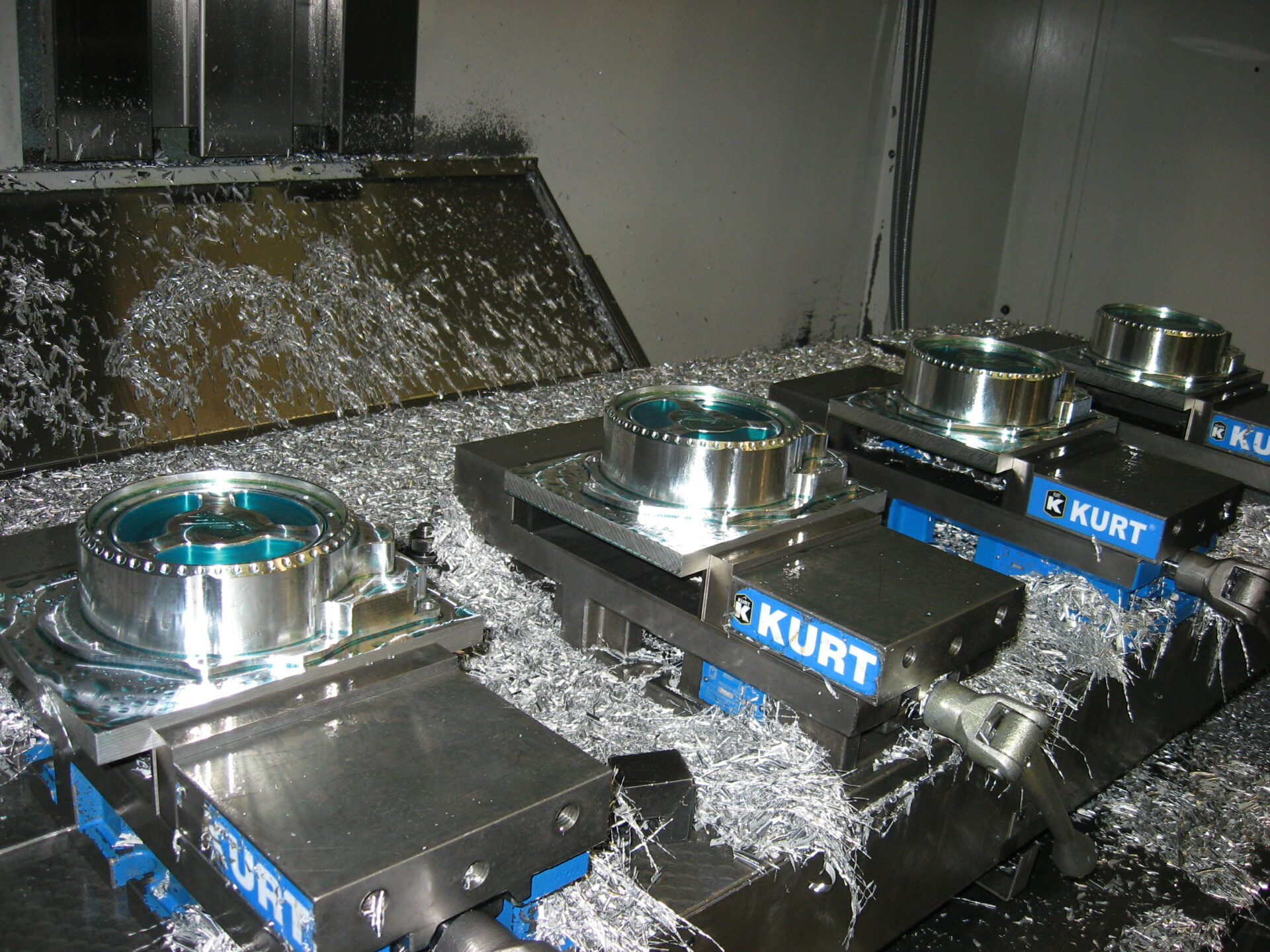 Four circular metal parts clamped in Kurt vises inside a CNC machine